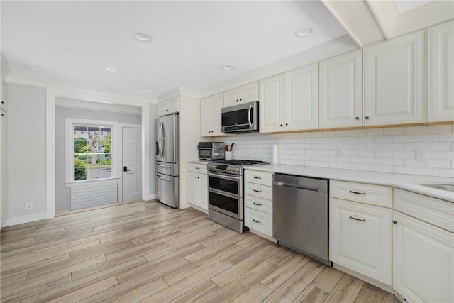 2 Carvin Ct, Warwick, RI 02886 - kitchen with appliances with stainless steel finishes, light countertops, backsplash, light wood-style flooring, and crown molding
