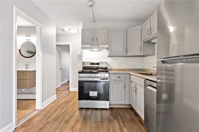 3940 Post Rd Unit 38, Warwick, RI 02886 - kitchen with stainless steel appliances, under cabinet range hood, decorative backsplash, light wood-type flooring, and light countertops