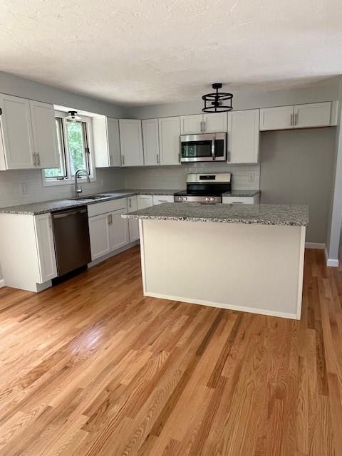 62 Lucille Dr, Woonsocket, RI 02895 - kitchen featuring appliances with stainless steel finishes, a sink, decorative backsplash, a kitchen island, and light stone countertops