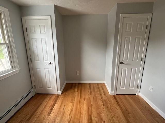 62 Lucille Dr, Woonsocket, RI 02895 - unfurnished bedroom with a baseboard heating unit, light wood finished floors, and baseboards