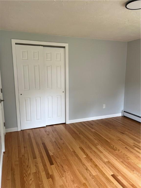 62 Lucille Dr, Woonsocket, RI 02895 - unfurnished bedroom featuring baseboard heating, baseboards, wood finished floors, a closet, and a textured ceiling