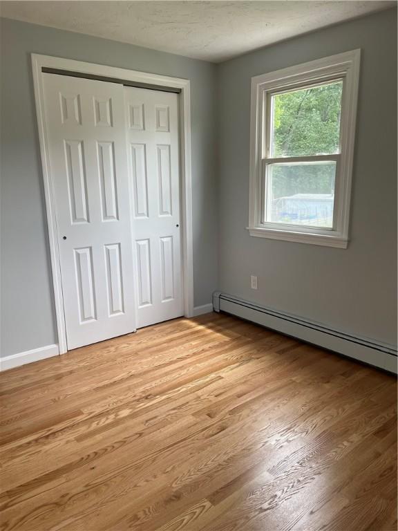 62 Lucille Dr, Woonsocket, RI 02895 - unfurnished bedroom featuring a baseboard radiator, a closet, light wood finished floors, and baseboards