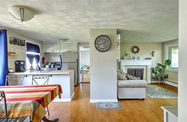 92 Chatworth Ave, Warwick, RI 02886 - kitchen with appliances with stainless steel finishes, a textured ceiling, white cabinets, a baseboard radiator, and light wood-style flooring