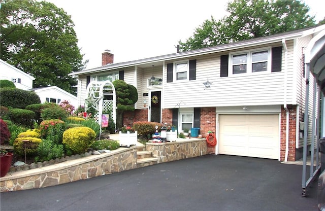 15 Ponderosa Dr, West Warwick, RI 02893 - split foyer home featuring a chimney, brick siding, asphalt driveway, and a garage