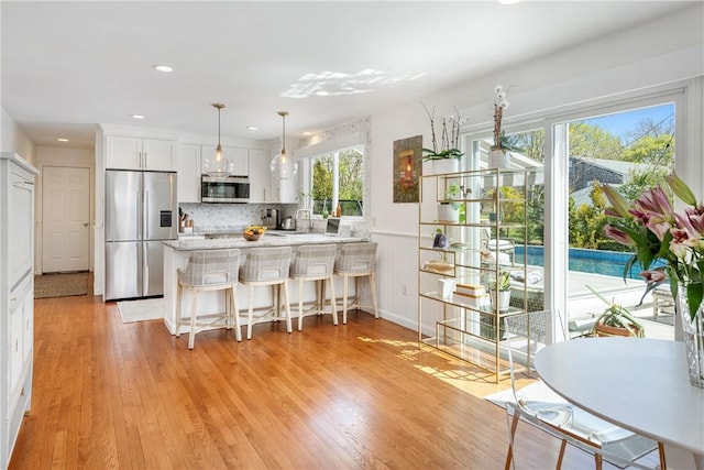 7 Maloney Ln, Middletown, RI 02842 - kitchen with appliances with stainless steel finishes, white cabinets, a peninsula, light wood-type flooring, and backsplash