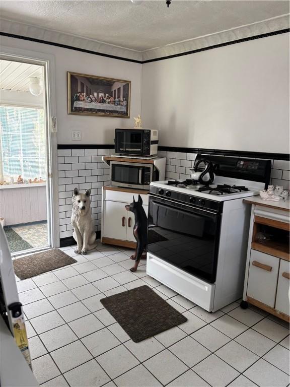 259 Park Ave, Woonsocket, RI 02895 - kitchen featuring white range with gas cooktop, stainless steel microwave, a textured ceiling, tile walls, and a wainscoted wall
