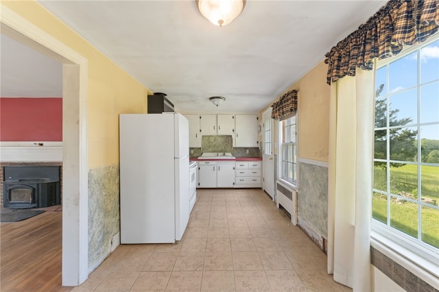 282 Seven Mile Rd, Scituate, RI 02831 - kitchen with freestanding refrigerator, radiator heating unit, a wood stove, white cabinets, and light tile patterned flooring