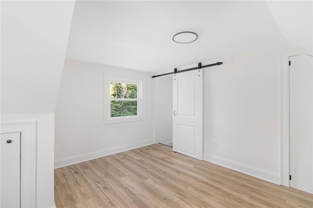 126 Weaver Hill Rd, West Greenwich, RI 02817 - unfurnished bedroom with a barn door, light wood-style flooring, and baseboards