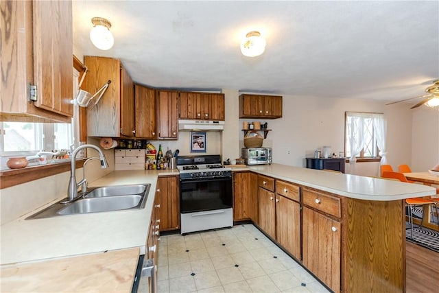 339 Beverage Hill Ave, Pawtucket, RI 02861 - kitchen featuring white gas range, under cabinet range hood, a sink, brown cabinetry, and light countertops