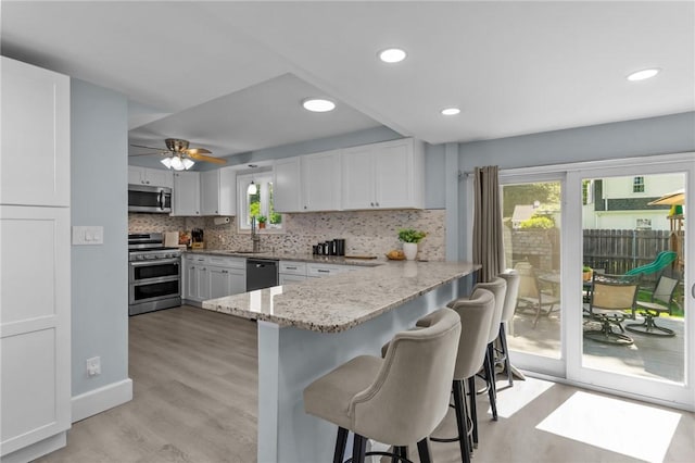 44 Felsmere Ave, Pawtucket, RI 02861 - kitchen with stainless steel appliances, a kitchen bar, light wood-style flooring, white cabinets, and backsplash