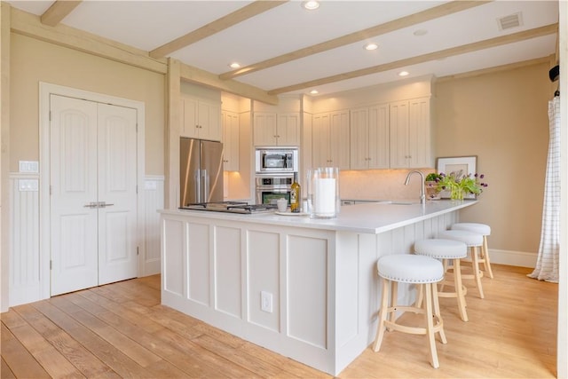 62 James Ct, Portsmouth, RI 02871 - kitchen featuring appliances with stainless steel finishes, a peninsula, a breakfast bar, light countertops, and light wood-style flooring
