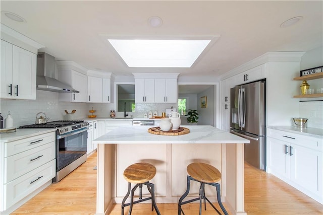24 W Knollwood Cir, North Kingstown, RI 02852 - kitchen featuring stainless steel appliances, wall chimney exhaust hood, a skylight, a kitchen bar, and backsplash