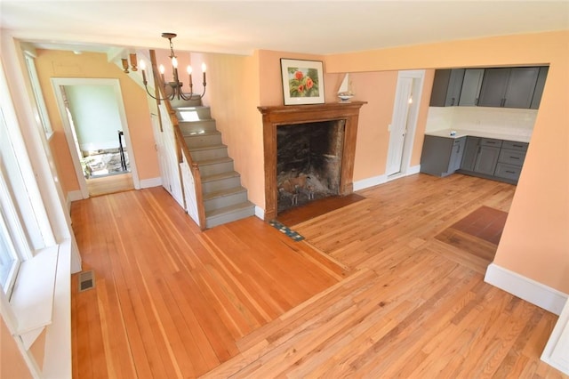259 Green Hill Beach Rd, South Kingstown, RI 02879 - unfurnished living room with a chandelier, light wood-style floors, stairs, a premium fireplace, and baseboards