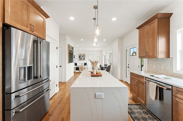51 Burnett Rd, Warwick, RI 02889 - kitchen with appliances with stainless steel finishes, light wood-type flooring, decorative backsplash, brown cabinetry, and a center island