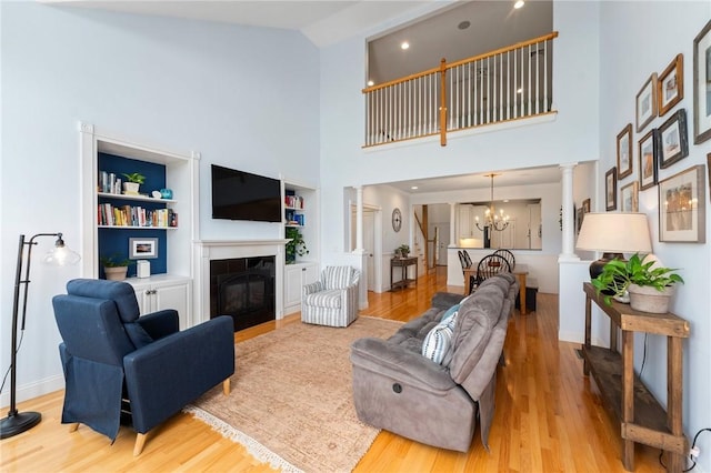83 Waters Edge St Unit 24, Tiverton, RI 02878 - living area with decorative columns, light wood-type flooring, a towering ceiling, a glass covered fireplace, and built in shelves