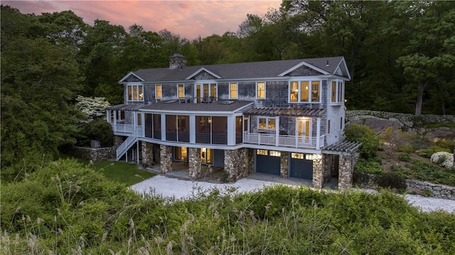 137 Cove Pt E, Charlestown, RI 02813 - back of property at dusk featuring stone siding, a garage, stairway, driveway, and a patio area