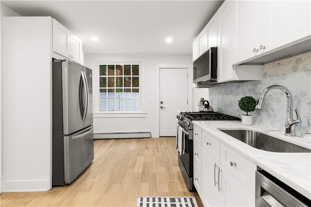 51 Poplar St Unit 1L, Newport, RI 02840 - kitchen featuring appliances with stainless steel finishes, a baseboard radiator, white cabinetry, decorative backsplash, and light wood-style flooring