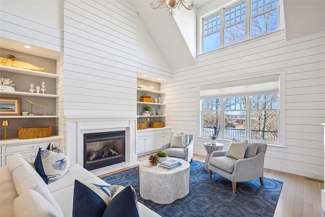 7 Spring Pond Rd, Westerly, RI 02891 - living room with hardwood / wood-style floors, wood walls, a glass covered fireplace, high vaulted ceiling, and a chandelier