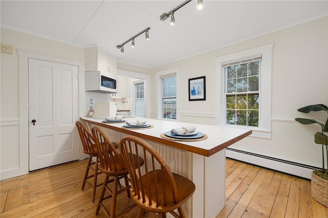 43 Cherry Ln Unit B, South Kingstown, RI 02879 - kitchen featuring a baseboard heating unit, white microwave, rail lighting, a breakfast bar area, and light wood-style flooring