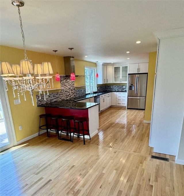 30 Hoover St, West Warwick, RI 02893 - kitchen with appliances with stainless steel finishes, a peninsula, tasteful backsplash, light wood-type flooring, and glass insert cabinets