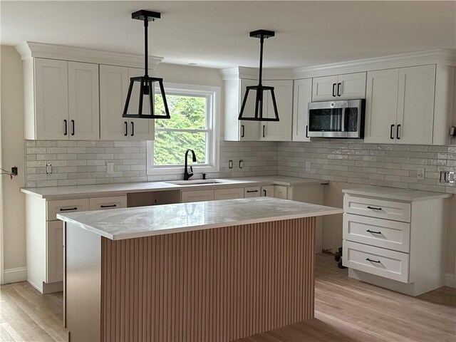 199 First Ave, East Greenwich, RI 02818 - kitchen featuring stainless steel microwave, light wood finished floors, decorative backsplash, and white cabinetry