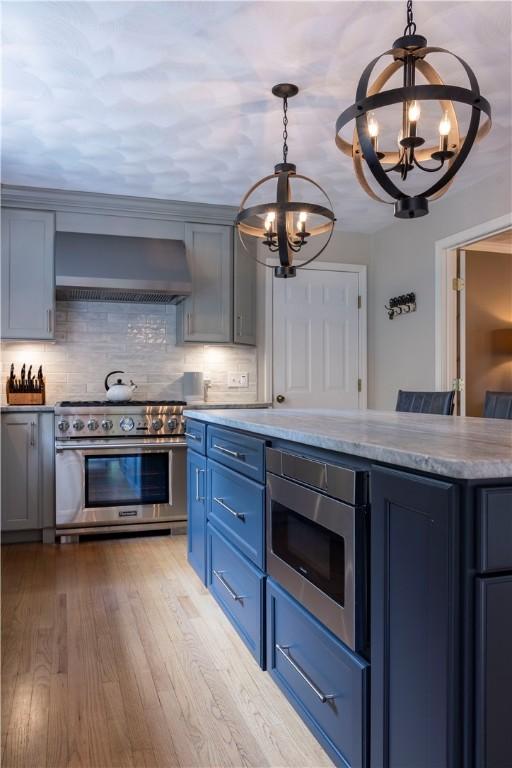 31 Wickaboxet Dr, West Greenwich, RI 02817 - kitchen with stainless steel appliances, wall chimney exhaust hood, a chandelier, blue cabinets, and decorative backsplash