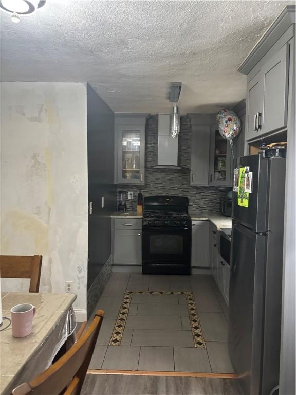 34 Lewis St, Central Falls, RI 02863 - kitchen with black range with gas cooktop, freestanding refrigerator, wall chimney exhaust hood, light countertops, and a textured ceiling