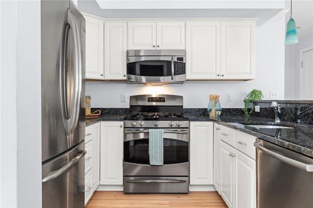 20 Narragansett Ave Unit 404, Narragansett, RI 02882 - kitchen featuring appliances with stainless steel finishes, white cabinetry, dark stone countertops, light wood finished floors, and decorative light fixtures