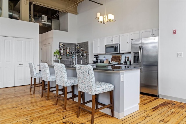 685 Social St Unit 114, Woonsocket, RI 02895 - kitchen featuring appliances with stainless steel finishes, a towering ceiling, white cabinetry, light wood finished floors, and a kitchen bar