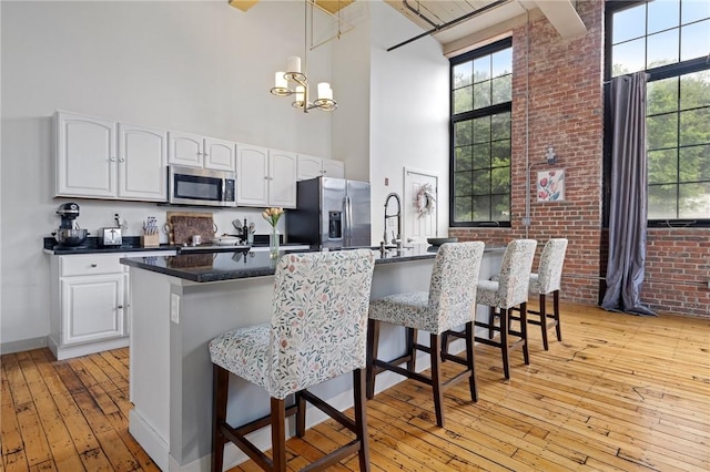 685 Social St Unit 114, Woonsocket, RI 02895 - kitchen with appliances with stainless steel finishes, a towering ceiling, light wood-style floors, white cabinetry, and a breakfast bar