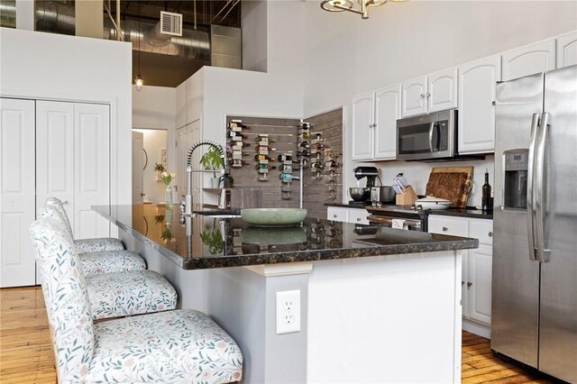 685 Social St Unit 114, Woonsocket, RI 02895 - kitchen featuring appliances with stainless steel finishes, a towering ceiling, light wood-type flooring, white cabinets, and a breakfast bar