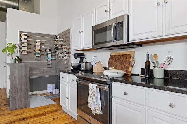 685 Social St Unit 114, Woonsocket, RI 02895 - kitchen featuring stainless steel microwave, electric range oven, white cabinetry, dark stone countertops, and light wood finished floors