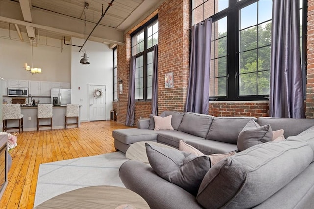 685 Social St Unit 114, Woonsocket, RI 02895 - living area featuring a high ceiling, brick wall, light wood finished floors, beam ceiling, and a chandelier