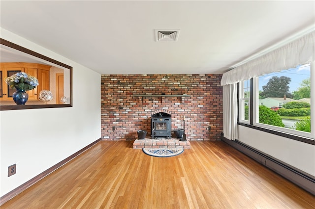 15 Rutland St, Warwick, RI 02888 - unfurnished living room featuring baseboard heating, a wood stove, wood finished floors, and brick wall
