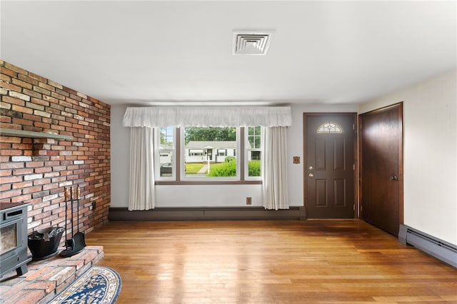 15 Rutland St, Warwick, RI 02888 - unfurnished living room featuring brick wall, a baseboard heating unit, light wood-style flooring, a wood stove, and a baseboard radiator
