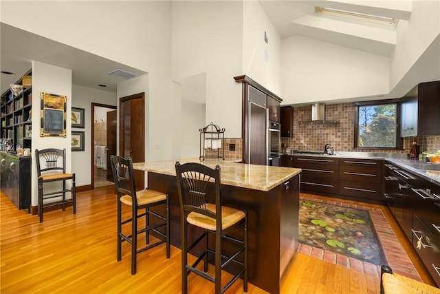 11 Mill Brook Ct, Charlestown, RI 02813 - kitchen featuring wall chimney exhaust hood, a towering ceiling, stainless steel counters, wood finished floors, and dark brown cabinets