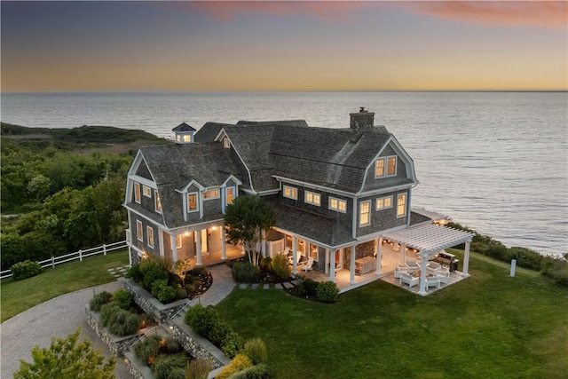 1210 Graces Cove Rd, Block Island, RI 02807 - back of house at dusk with a water view, a gambrel roof, a chimney, a patio, and a garage