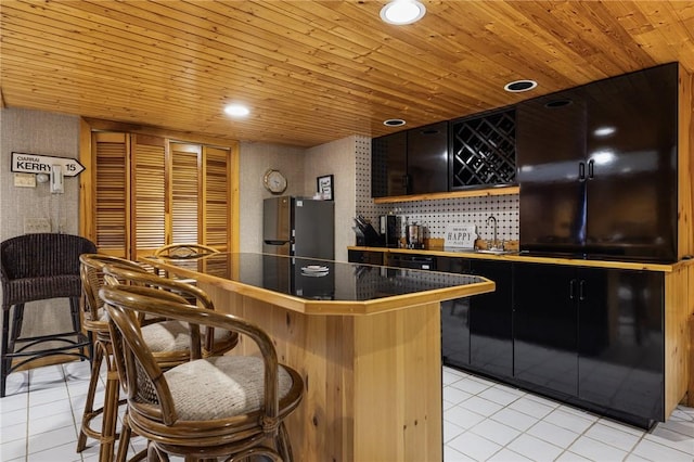 788 Namquid Dr, Warwick, RI 02888 - kitchen featuring freestanding refrigerator, light tile patterned floors, a kitchen bar, dark cabinets, and wooden ceiling