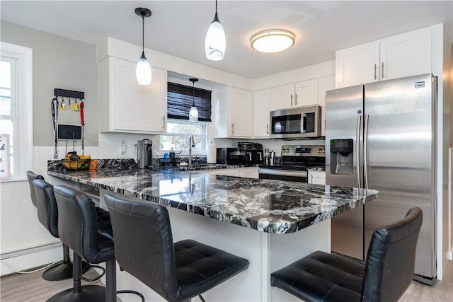 111 Belgium St, Cranston, RI 02920 - kitchen featuring stainless steel appliances, a peninsula, white cabinets, dark stone counters, and light wood-style flooring