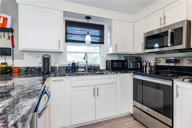 111 Belgium St, Cranston, RI 02920 - kitchen with stainless steel appliances, white cabinets, dark stone counters, hanging light fixtures, and light wood-style flooring