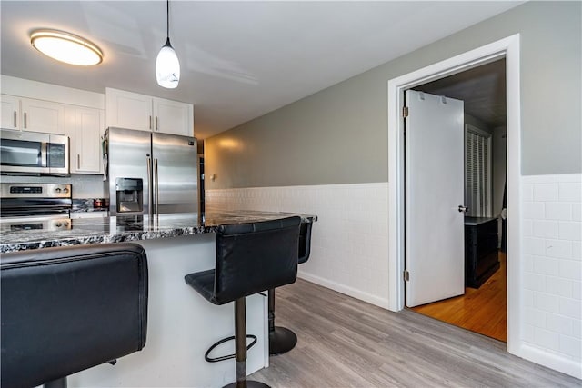 111 Belgium St, Cranston, RI 02920 - kitchen with stainless steel appliances, tile walls, a wainscoted wall, a kitchen breakfast bar, and light wood-style flooring