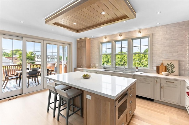 35 Coggeshall Ave, Newport, RI 02840 - kitchen with stainless steel microwave, a tray ceiling, a center island, light wood-style flooring, and decorative backsplash