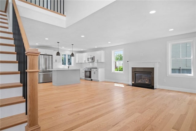 52 Governor St, Cumberland, RI 02864 - unfurnished living room featuring recessed lighting, light wood-type flooring, stairway, a fireplace with flush hearth, and plenty of natural light