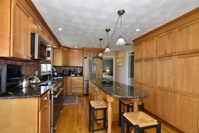 1 Butts Rock Rd, Little Compton, RI 02837 - kitchen featuring appliances with stainless steel finishes, a center island, light wood finished floors, tasteful backsplash, and a kitchen bar