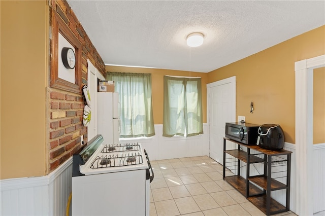 313 Branch Ave, Providence, RI 02904 - kitchen with white appliances, wainscoting, a textured ceiling, a decorative wall, and light tile patterned floors