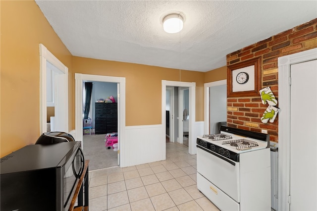 313 Branch Ave, Providence, RI 02904 - kitchen featuring white gas range oven, a textured ceiling, a wainscoted wall, brick wall, and light tile patterned floors
