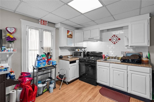 233 Waterman Ave, East Providence, RI 02914 - kitchen with black gas range oven, under cabinet range hood, stainless steel microwave, a drop ceiling, and white cabinetry