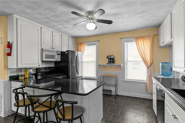 167 Carter Ave, Pawtucket, RI 02861 - kitchen with white microwave, black gas range, freestanding refrigerator, white cabinets, and a peninsula