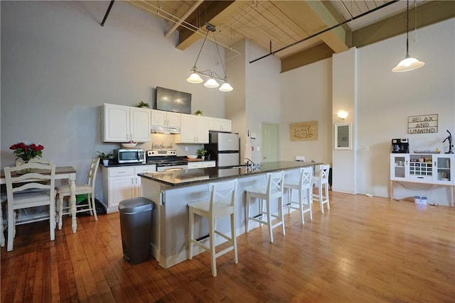 685 Social St Unit 103, Woonsocket, RI 02895 - kitchen featuring freestanding refrigerator, stainless steel microwave, a high ceiling, dark countertops, and under cabinet range hood