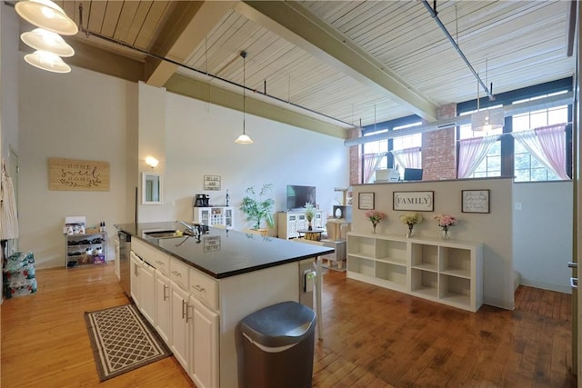 685 Social St Unit 103, Woonsocket, RI 02895 - kitchen featuring beamed ceiling, dark countertops, white cabinets, light wood-style flooring, and an island with sink